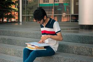 un joven estudiante con una camiseta y gafas leyendo en un libro de cara foto