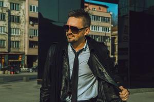 Fashionable male model looking away with sunglasses and leather jacket photo