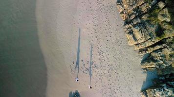 pareja feliz corriendo en la orilla de una playa de arena en praia de caion, españa. aéreo de arriba hacia abajo
