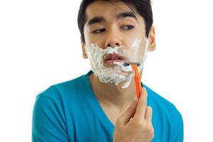 funny and charming guy in the blue shirt looks away and shaves his beard with foam and shaving machine photo