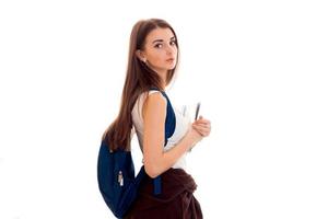 joven estudiante cansada con mochila azul en el hombro y carpetas para cuadernos en las manos mirando la cámara aislada de fondo blanco foto