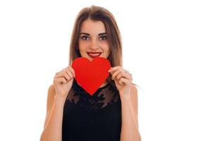 a charming young girl in a black dress smiles and holding a red heart isolated on white background photo