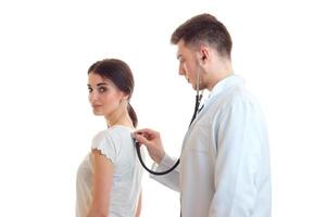 a young doctor in a white lab coat with a stethoscope is listening back at girl close-up photo