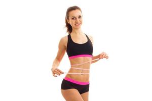 cute athletic girl in black top takes the waist measuring tape and smiling photo