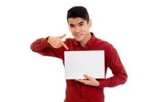 Un joven moreno de moda posando con un cartel vacío en las manos y sonriendo a la cámara aislado de fondo blanco foto