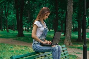 young brunette girl sits on a bench and wotking with laptop photo