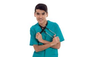 joven médico con traje azul sosteniendo las manos estetoscopio alrededor de su cuello y mirando fijamente a la cámara aislada en fondo blanco foto