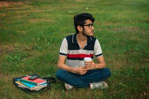 young charming guy sits on a green lawn holds a cup of coffee photo