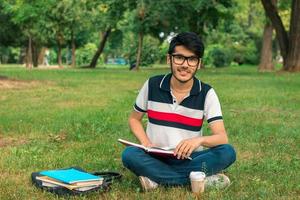 beautiful smiling guy in glasses sitting on the grass with books photo