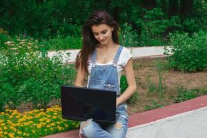 una joven sonriente se sienta en el parque e imprime en una laptop foto