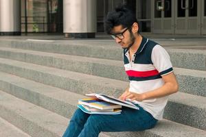 un joven encantador está sentado en las escaleras y lee libros foto