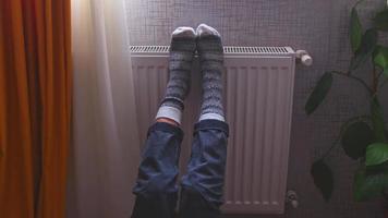 ben med färgrik stickat vinter- xmas strumpor på fötter uppvärmningen på central uppvärmning radiator värmare. vinter- tid, kall väder säsong fester ensamhet på Hem ensam video