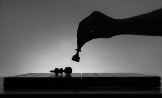 Chess board with chess pieces silhuettes on white background. Concept of business ideas, competition and strategy ideas. Black and White art photo. Chess player hand. Weak king was defeated. Checkmate photo