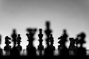 Chess board with chess pieces silhuettes on white background. Concept of business ideas, competition and strategy ideas. Black and White classic art photo. All figure ready for battle, before opening photo