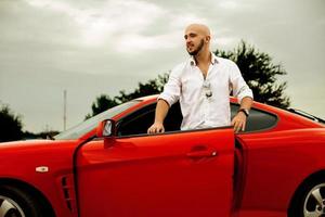 un hombre guapo sale de un auto deportivo rojo foto