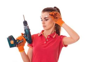 Cutie joven morena builder chica en uniforme y gafas hace renovación con taladro en manos aislado sobre fondo blanco. foto