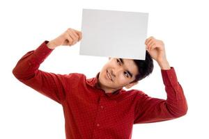 un joven gracioso y elegante con camisa roja posando con una pancarta vacía en las manos y mirando hacia arriba aislado de fondo blanco foto