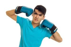 angry brunette sportsman in blue boxing gloves and uniform practicing boxing isolated on white background photo