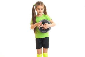 pequeña niña con una camiseta brillante y colas sostiene la pelota en el estudio foto