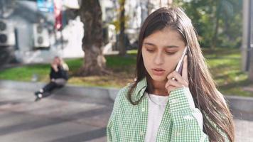 Woman talks on phone on sunny sidewalk video