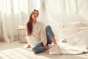 Charming woman sits in front of bed at light room at home photo