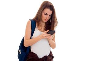 young girl in white shirt and with a backpack on her shoulder holds mobile phone photo