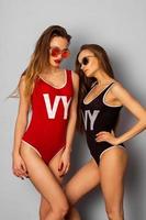 two young sexy girls in body swimsuit and sunglasses in studio photo