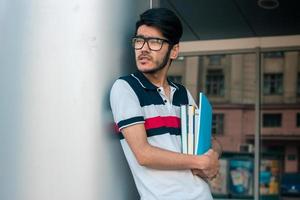 handsome student with books in hands wears a glasses and looks aside photo