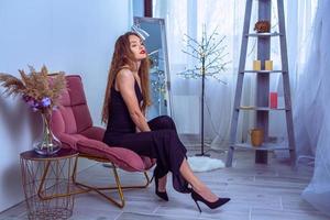 Beautiful woman in black overalls on high heels sits on a chair photo