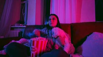 une femme réagit au film alors qu'elle est assise sur un canapé avec du pop-corn