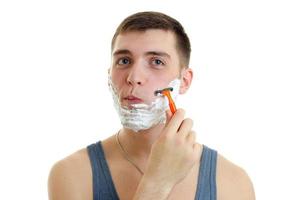 Portrait of a ridiculously young guy with foam on his face who shaves his beard machine photo