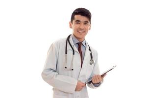 feliz médico masculino en uniforme con estetoscopio hace notas aisladas sobre fondo blanco foto