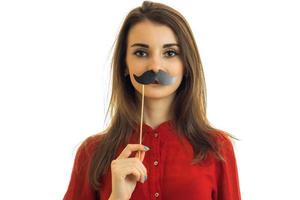 a young girl in a red blouse keeps near the mouth paper mustache is isolated on a white background photo
