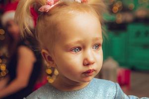 close up portrait of little baby girl looking away with xmas tree behind her photo