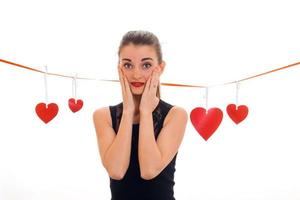 young surprised brunette lady with red heart in studio smiling on camera isolated on white background. Valentines Day concept. photo