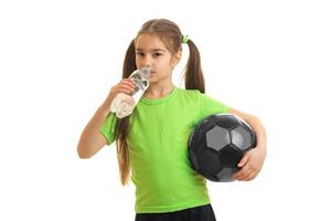 Petite athletic girl holding a ball and drink water from a bottle photo