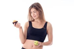 Fitness girl in black top holds a cupcake and Apple isolated on white background photo