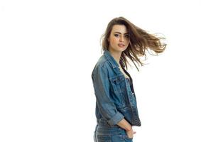 linda joven con chaqueta de jeans mira a la cámara y su cabello vuela por el aire foto