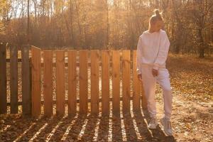 girl stands near a wooden fence in the fall photo