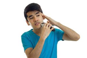 a young guy in the blue shirt shaves his face and looks toward photo