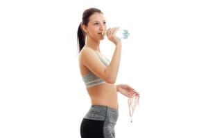 Athletic beautiful slender girl stands sideways in a gray top and drinking mineral water photo