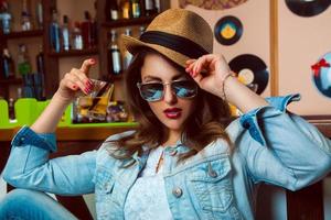 Young adult woman in sunglasses drink cocktail in bar photo