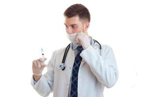 a young doctor in a lab coat with a mask on his face holding a syringe photo