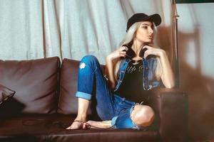 Serious young beautiful blond woman in casual clothes posing on couch and looking away photo