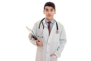 un joven médico con una bata blanca de laboratorio con un estetoscopio sosteniendo una tableta para valores foto