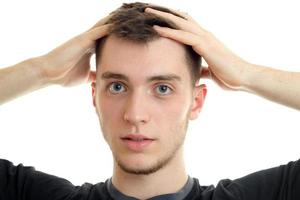 retrato de un hombre guapo y encantador que mira a la cámara y sostiene la cabeza de las manos aislada en el fondo blanco foto