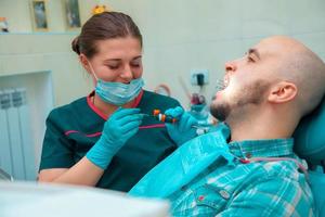 retrato horizontal de la hermosa morena dentista trata los dientes en su paciente foto
