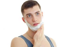 Portrait of a remarkable young man who looks away and shaving foam on beard close-up photo