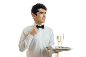 charming young waiter smiles corrects hand bow tie and holds a tray with glasses of wine photo