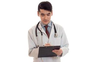 young male doctor in uniform with stathoscope makes notes isolated on white background photo